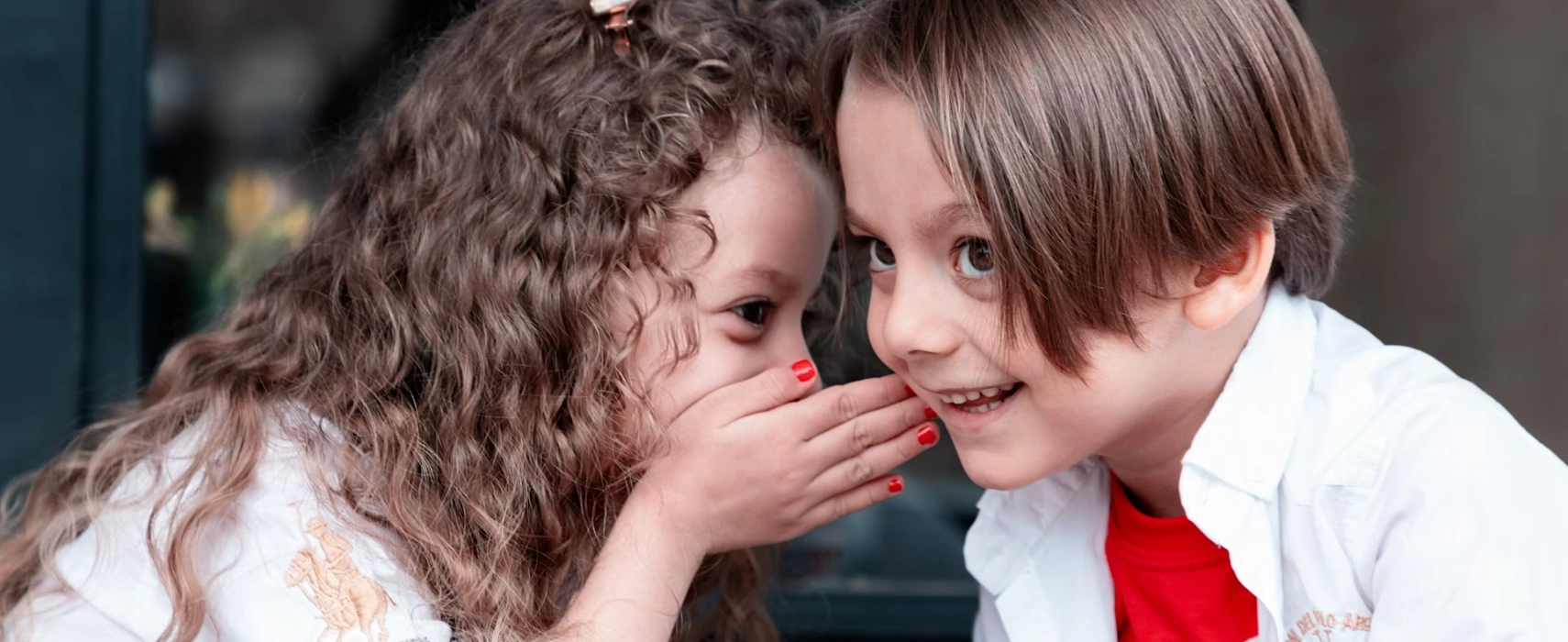 Young girl telling a secret to a young boy